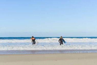 Erkek ve kadın sörf tahtaları ile okyanusa gidin. Erkek ve kız sörf, Portekiz, Nazar gidin. Islati takım elbiseyle sörf.