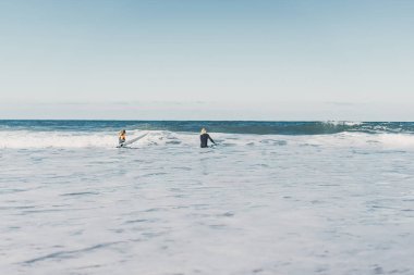 Erkek ve kadın sörf tahtaları ile okyanusa gidin. Erkek ve kız sörf, Portekiz, Nazar gidin. Islati takım elbiseyle sörf.