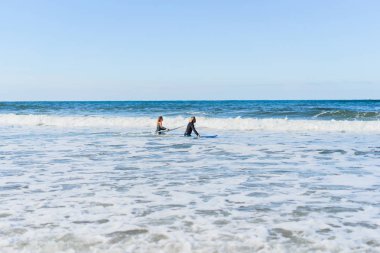 Erkek ve kadın sörf tahtaları ile okyanusa gidin. Erkek ve kız sörf, Portekiz, Nazar gidin. Islati takım elbiseyle sörf.