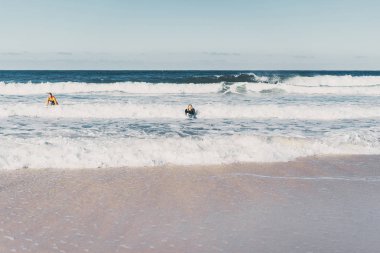 Erkek ve kadın sörf tahtaları ile okyanusa gidin. Erkek ve kız sörf, Portekiz, Nazar gidin. Islati takım elbiseyle sörf.