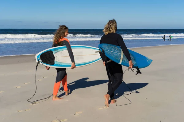 man and woman go to the ocean with surf boards. man and girl go surfing, Portugal, Nazar. Surfing in a wet suit.