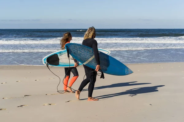 man and woman go to the ocean with surf boards. man and girl go surfing, Portugal, Nazar. Surfing in a wet suit.