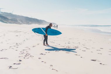 okyanus kıyısında sörf tahtası olan adam. Sörfçü ıslak elbiseli. Nazare, Portekiz.