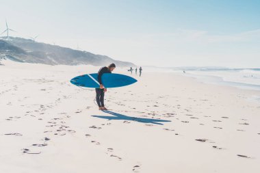 okyanus kıyısında sörf tahtası olan adam. Sörfçü ıslak elbiseli. Nazare, Portekiz.