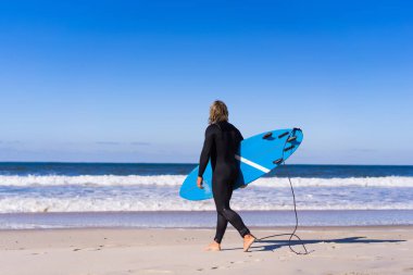 okyanus kıyısında sörf tahtası olan adam. Sörfçü ıslak elbiseli. Nazare, Portekiz.