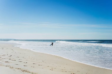 okyanus kıyısında sörf tahtası olan adam. Sörfçü ıslak elbiseli. Nazare, Portekiz.