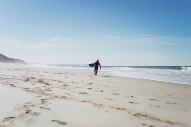 okyanus kıyısında sörf tahtası olan adam. Sörfçü ıslak elbiseli. Nazare, Portekiz.