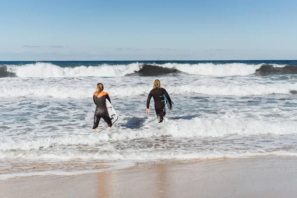 man and woman go to the ocean with surf boards. man and girl go surfing, Portugal, Nazar. Surfing in a wet suit.