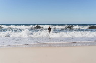 Palet ve okyanus kıyısında hidro elbiseli bir bodyboard sörfçü