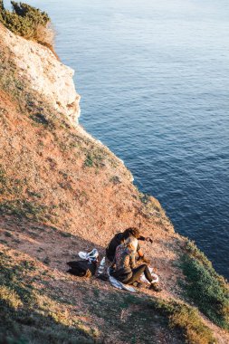 gün batımında, seven çift kaya kenarında oturur ve okyanus ve gün batımı manzarasına sahiptir.