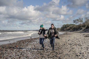 genç bir çift hafta sonları deniz kenarı soğuk Baltık Denizi, kumsalı, sıcak ceketler, Aile hafta sonu erkek ve kadın plajda çalışan harcama aşık.