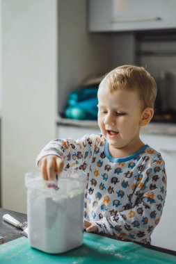 Çocuk pijamalı, annesi mutfakta elmalı turta pişiriyor ve oyuncaklarla oynuyor.