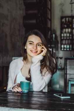 büyüleyici bir gülümseme ve kahve içme ve bir smartphone kullanarak ifade kahverengi gözlü güzel bir esmer kız