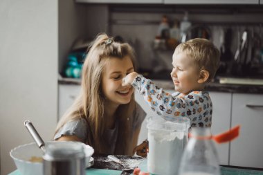 Çocuk pijamalı, annesi mutfakta elmalı turta pişiriyor ve oyuncaklarla oynuyor.