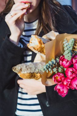 Genç güzel kız Fransız kadın esmer kırmızı bere ve siyah bir ceket Avrupa şehri Street'te bir buket çiçek ve Fransız baget ile gider. Mutlu bir gülümseme ve büyüleyici bir bak, Paris Fransız tarzı