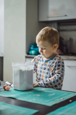 Çocuk pijamalı, annesi mutfakta elmalı turta pişiriyor ve oyuncaklarla oynuyor.