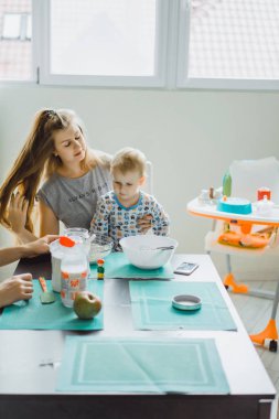 Çocuk pijamalı, annesi mutfakta elmalı turta pişiriyor ve oyuncaklarla oynuyor.