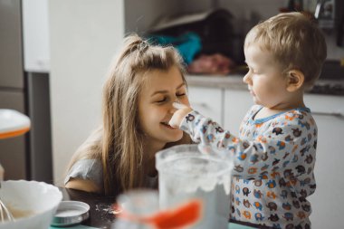 Çocuk pijamalı, annesi mutfakta elmalı turta pişiriyor ve oyuncaklarla oynuyor.