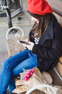 kırmızı bere güzel esmer kadını sokakta bankta oturur, selfie yapar, bir akıllı telefon kullanır