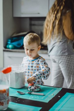 Çocuk pijamalı, annesi mutfakta elmalı turta pişiriyor ve oyuncaklarla oynuyor.