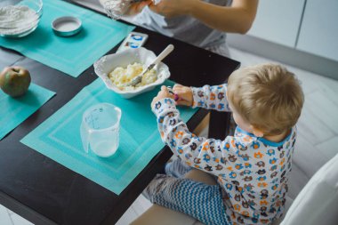 Çocuk pijamalı, annesi mutfakta elmalı turta pişiriyor ve oyuncaklarla oynuyor.