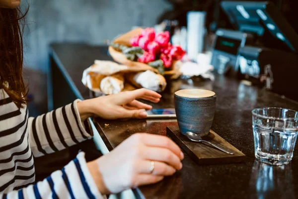 A mug with coffee cappuccino on the table in a cafe. Smartphone, bouquet of flowers and cappuccino. Organization of space on the table