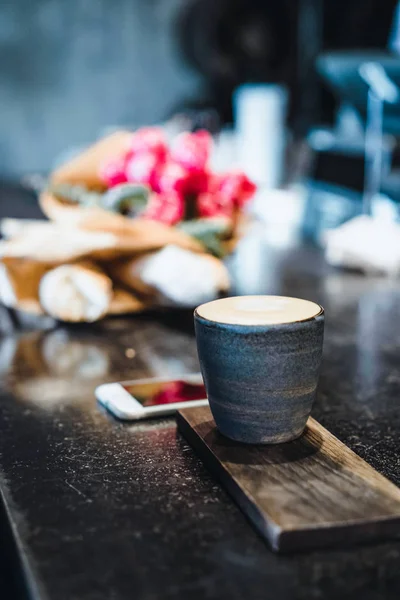 A mug with coffee cappuccino on the table in a cafe. Smartphone, bouquet of flowers and cappuccino. Organization of space on the table
