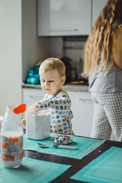 Çocuk pijamalı, annesi mutfakta elmalı turta pişiriyor ve oyuncaklarla oynuyor.