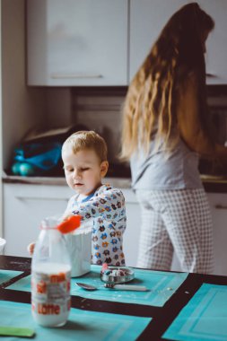 Çocuk pijamalı, annesi mutfakta elmalı turta pişiriyor ve oyuncaklarla oynuyor.