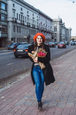 Genç güzel kız Fransız kadın esmer kırmızı bere ve siyah bir ceket Avrupa şehri Street'te bir buket çiçek ve Fransız baget ile gider. Mutlu bir gülümseme ve büyüleyici bir bak, Paris Fransız tarzı