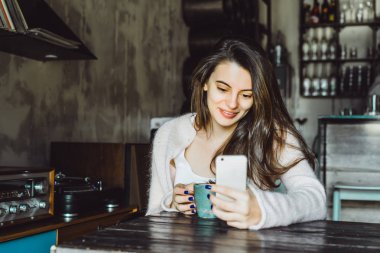 büyüleyici bir gülümseme ve kahve içme ve bir smartphone kullanarak ifade kahverengi gözlü güzel bir esmer kız