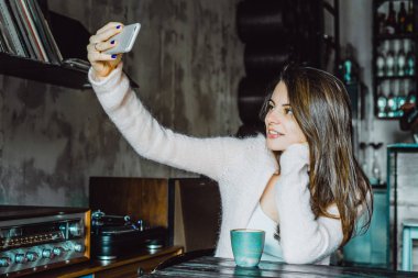 büyüleyici bir gülümseme ve kahve içme ve bir smartphone kullanarak ifade kahverengi gözlü güzel bir esmer kız