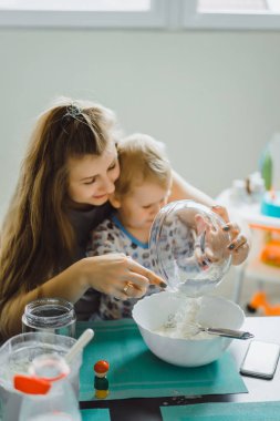 Çocuk pijamalı, annesi mutfakta elmalı turta pişiriyor ve oyuncaklarla oynuyor.