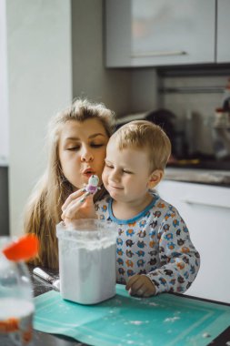 Çocuk pijamalı, annesi mutfakta elmalı turta pişiriyor ve oyuncaklarla oynuyor.