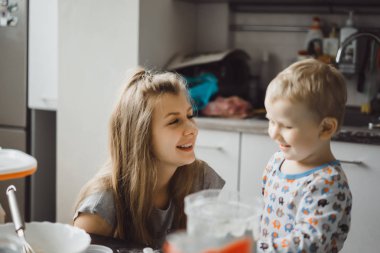 Çocuk pijamalı, annesi mutfakta elmalı turta pişiriyor ve oyuncaklarla oynuyor.