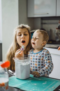 Çocuk pijamalı, annesi mutfakta elmalı turta pişiriyor ve oyuncaklarla oynuyor.