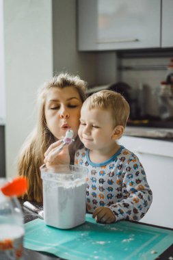 Çocuk pijamalı, annesi mutfakta elmalı turta pişiriyor ve oyuncaklarla oynuyor.