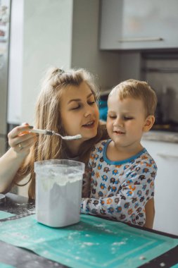 Çocuk pijamalı, annesi mutfakta elmalı turta pişiriyor ve oyuncaklarla oynuyor.