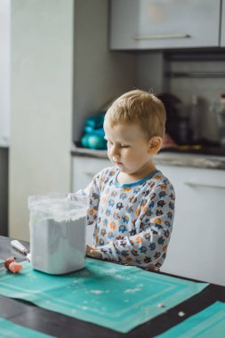 Çocuk pijamalı, annesi mutfakta elmalı turta pişiriyor ve oyuncaklarla oynuyor.