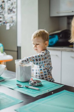 Çocuk pijamalı, annesi mutfakta elmalı turta pişiriyor ve oyuncaklarla oynuyor.