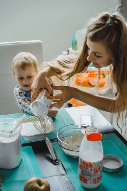 Çocuk pijamalı, annesi mutfakta elmalı turta pişiriyor ve oyuncaklarla oynuyor.