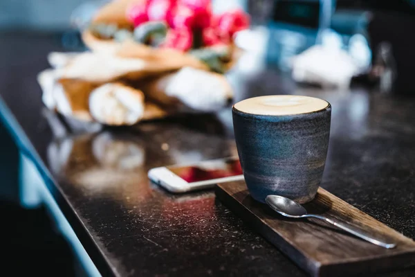 A mug with coffee cappuccino on the table in a cafe. Smartphone, bouquet of flowers and cappuccino. Organization of space on the table