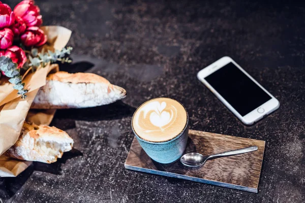 A mug with coffee cappuccino on the table in a cafe. Smartphone, bouquet of flowers and cappuccino. Organization of space on the table