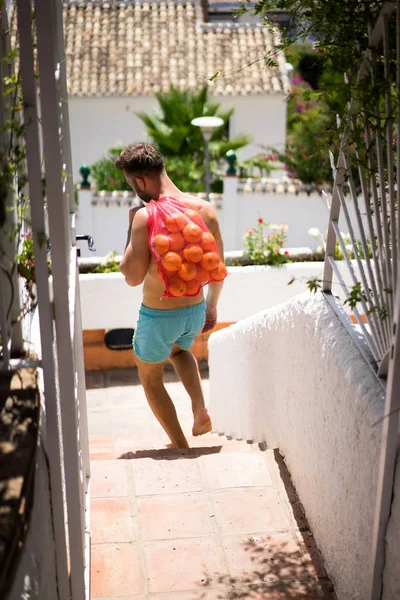 a man with a bare-chested bears a bag of oranges. Spain