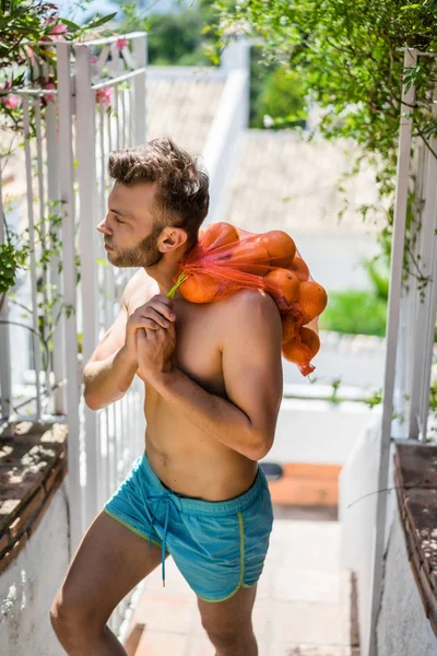 a man with a bare-chested bears a bag of oranges. Spain