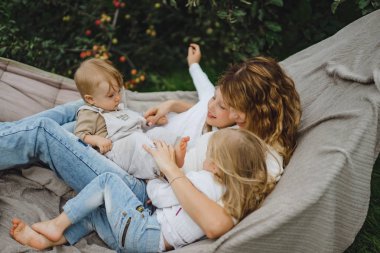 bir hamakta eğleniyor çocuk anne. Anne ve çocuklar bir hamak. Aile ile çocuk bahçesinde vakit geçiriyor.