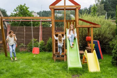 Anne ve kızı bir salıncak ve bir çocuk slayt üzerinde zaman harcıyor. Annesiyle beraber çocuklar zaman.