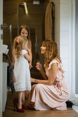Anne ve kızı banyoda makyaj yapmak, aynanın önünde ruj uygulayın. Kızı annesinin topuklar. Anne ve kızı birlikte vakit geçirmek iyi eğlenceler.