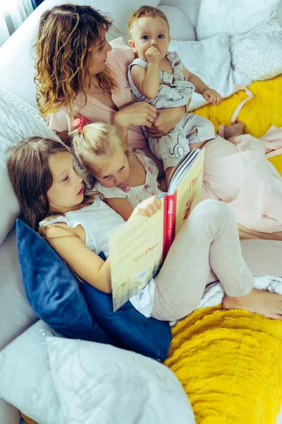 mother with three children reading a book in a homely atmosphere, sharing time with parents and children. mother, two daughters and a little son.