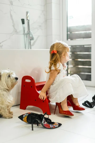 Mom and daughters do makeup in the bathroom, apply lipstick in front of the mirror. Daughters in her mother\'s heels. Mom and daughters have fun, spend time together.